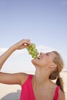 Side view of happy woman holding bunch of grapes near mouth