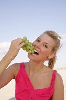 Portrait of blonde woman holding bunch of grapes and eating, smiling