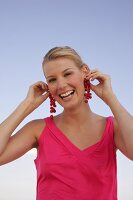 Frau in pinkem Top hält sich Johannisbeeren an ihre Ohren