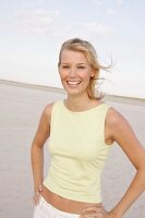 Frau mit blonden Haaren, steht lachend an windigem Strand