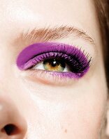 Close-up of woman's eye wearing fake eyelashes and purple eye shadow
