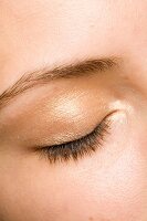 Extreme close-up of woman's closed eye wearing golden eye shadow