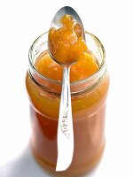 Glass jar of peach and mango jam with spoon on it