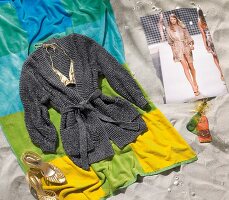 Gray cardigan on bath towel and golden sandals on sand