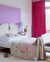 White bed with headboard against purple coloured wall with red curtain