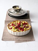 Berry tart in ramekin with stack of plates and cutlery on a piece of cloth