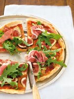 Slices of round pizza with arugula salad, parma ham, figs on plate