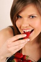 Frau mit langen Haaren isst Erdbeere mit Hand