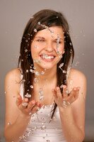 Close-up of pretty woman with brown hair cleaning her face with water, smiling