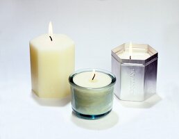 Close-up of three lit candles in hexagon glass and tin can on white background
