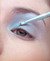 Close-up of woman applying silver eye shadow with a brush