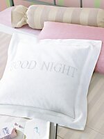 Kissen in Weiß mit Aufschrift "Good Night" auf Bett, andere Kissen rosa