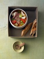 Bowl of parsnip and leek stew with lamb and slices of bread in box