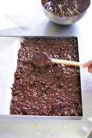 Close-up of chef spreading chocolate mixture on baking sheet with wooden spoon