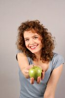 Frau hält Apfel in der Hand in die Kamera und lacht