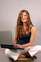 Beautiful woman with long curly hair in blue top sitting with laptop
