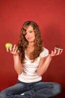 Pretty woman sitting cross legged holding green apple in one hand and muffin in other