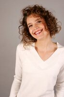 Portrait of beautiful woman with curly hair wearing white sweater, smiling widely