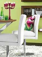Dining table with green-purple decorations and white swivel chairs in leather upholstery