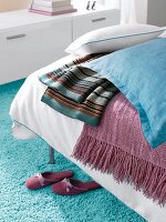 Kissen und Decken in Blau und Lila auf Bett in Weiß
