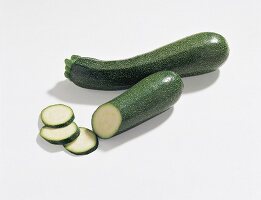 Whole and sliced dark green zucchini on white background