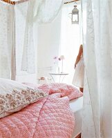Four poster bed with pink quilt and pillow