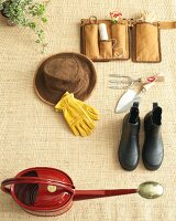 Hat, watering can, protective gloves, boots and gardening equipment on rug, elevated view