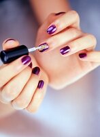 Close-up of woman applying gold dust on purple nail polish