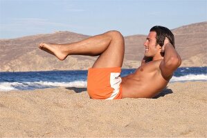 Mann macht Bauchmuskelübungen am Strand