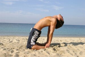 Mann macht Gymnastik am Strand, biegt den Rücken nach hinten