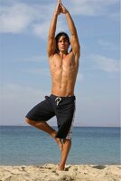 Mann macht Yogaübung am Strand, 'Der Baum'