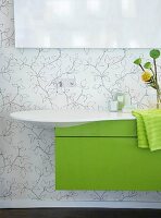 Weißes Waschbecken mit grünem Wascht isch, darüber Spiegel, geblümte Wand