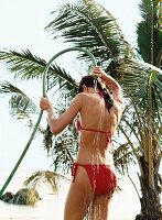 Rückansicht: Frau im roten Bikini du scht sich mit Wasserschlauch ab