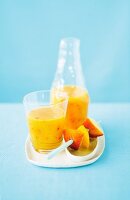 A mango and peach smoothie in a glass and in a bottle