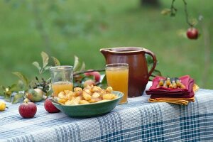 A bowl of apple compote and apple juice in an earthenware jug and in glasses on a table outside