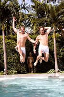 Men with shirtless jumping into the pool with palm trees in background