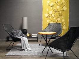 And elegant lounge area in grey and yellow – wicker chairs around a small round table with a golden yellow silk hanging in the background