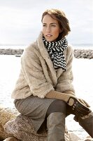 Contemplative woman wearing fur jacket and scarf sitting on stone, looking away
