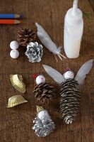 Weihnachtliches Bastelmaterial - Tannenzapfen, Federn, Klebstoff und Kugeln auf Holzablage