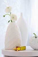 weiße Ranunkeln in Vase mit weisser Strickhülle
