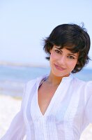 Portrait of beautiful woman with short hair in white blouse standing on beach, smiling