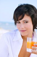 Brunette woman on beach holding glass of juice in hand