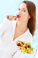 Frau isst Erdbeere von einem bunten Obstteller