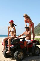 Two women and one man wearing swimsuit sitting on dune buggy and enjoying at beach