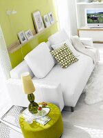 White leather couch in front of green wall and lamp on green side table besides it