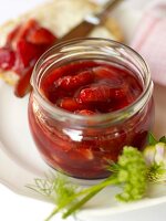 Glass jar with strawberry jam on plate