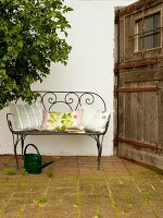 Garden filigree bench with pillows and watering can by side