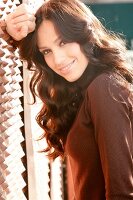 Portrait of beautiful dark haired woman wearing brown turtleneck leaning against wall