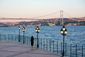 Rear view of woman standing near sea, overlooking city at sunset, Istanbul, Turkey