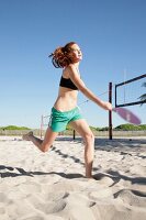 Young woman with red hair playing racket on beach